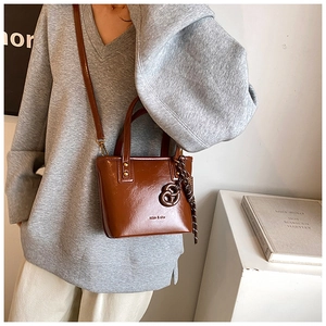 Détail d'un sac seau marron avec deux poignées et un pendentif décoratif en cuir noué