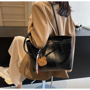 Detail of black tote bag featuring contrast white stitching and cute brown bear charm