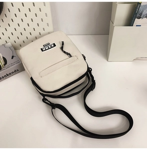 Détail du sac bandoulière ivoire avec sangle réglable noire et écusson de la marque