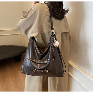 Detail of a large dark brown faux leather tote bag with metal buckles and baseball charm