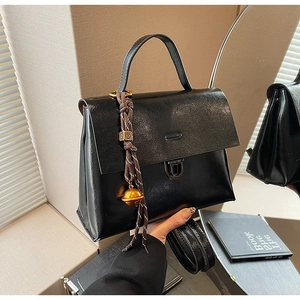 Détail d'un sac à main noir en cuir avec fermoir métallique et pendentif tressé chic