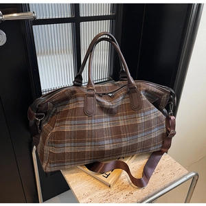 Détail du sac de voyage à carreaux avec poignées en cuir marron et bandoulière réglable