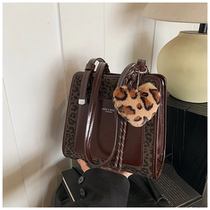Detail view of large brown leopard print tote bag with plush heart charm and logo