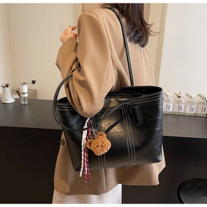 Close-up of black leather tote bag featuring white contrast stitching and bear charm