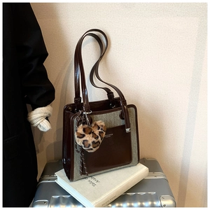 Close-up of contrast leather tote with leopard heart charm on a white book