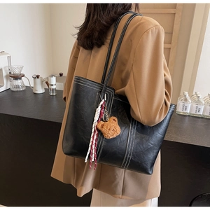 Detail of black tote bag with white stitching and bear charm on female model
