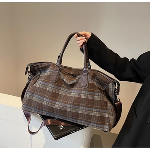 Détail du sac de voyage à carreaux montrant le tissu brun et les poignées en cuir