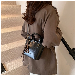 Vue détaillée du sac seau en cuir verni noir avec charm biscuit et bandoulière fine