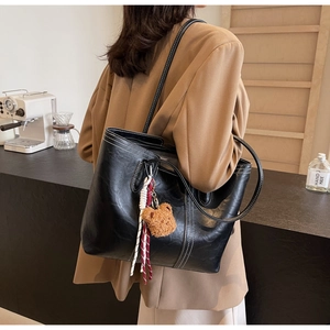 Detail of black tote bag with white stitching and bear charm worn on shoulder