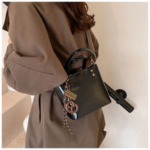 Vue détaillée du sac seau en cuir verni noir avec fini brillant et breloque dorée