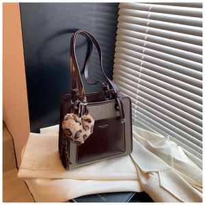 Close-up of contrast color tote bag with leopard heart charm on a cream blazer