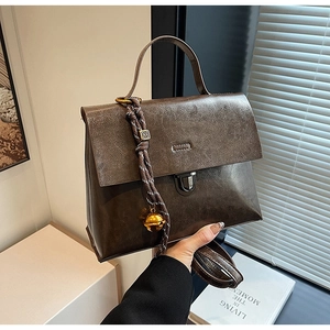 Détail d'un sac en cuir marron foncé avec un charme en corde tressée et clochette d'or