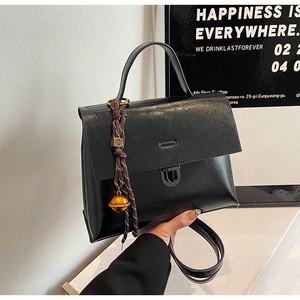 Détail du sac à main en similicuir noir avec breloque cloche tressée et fermoir en métal
