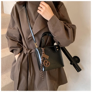 Détail d'un sac seau en cuir verni noir avec boulier doré et breloque tressée