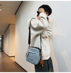 Détail du sac bandoulière bleu clair avec sangle noire et breloque pompon marron
