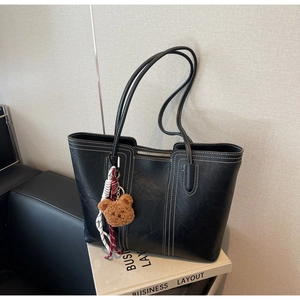 Detail of black tote bag featuring white contrast stitching and cute bear charm