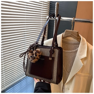Detail of contrast tote bag with leopard plush heart charm on a metal display stand