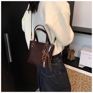 Détail d'un sac seau marron foncé brillant avec cordon tressé et rivets dorés sur modèle