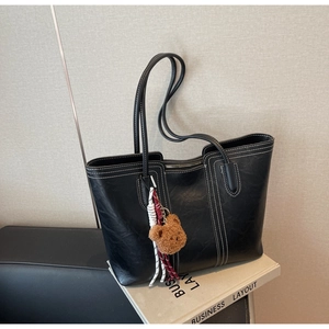 Close-up of black tote bag featuring contrast white stitching and a plush bear charm detail