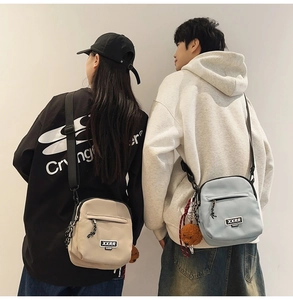 Détail de deux sacs bandoulière en blanc cassé et bleu clair avec pendentif ourson