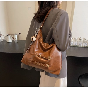 Detail of a large brown leather tote bag with buckle straps and a baseball pendant