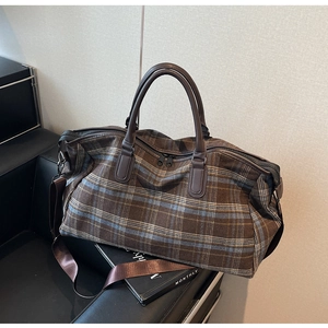 Détail d'un sac de voyage à carreaux avec poignées en cuir et bandoulière amovible