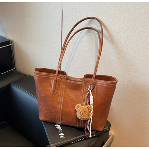 Detail of brown faux leather tote bag featuring white contrast stitching and a bear charm