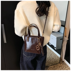 Détail d'un sac seau marron foncé brillant avec breloque nœud et clous dorés élégants