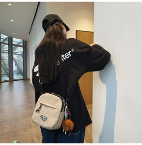 Détail du sac bandoulière beige en nylon avec logo XXRR et porte-clés ours en peluche