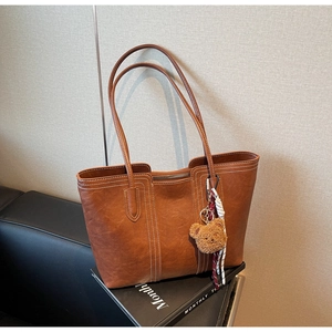Detail of a brown tote bag with white stitching, leather texture and a plush bear charm