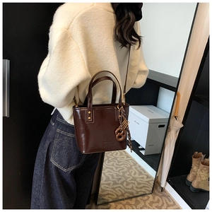 Détail du sac cabas en cuir verni marron foncé avec finition brillante et nœud décoratif