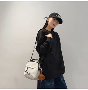 Détail d'un sac bandoulière en toile blanche avec étiquette XXRR et breloque chien