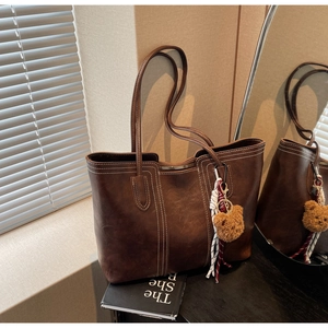 Close-up of brown tote bag featuring contrast white stitching and a cute bear charm