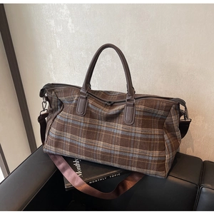 Détail d'un sac de voyage à carreaux marron avec poignées en cuir et bandoulière