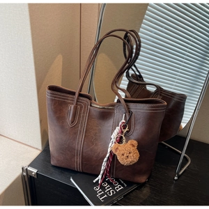 Macro shot of dark brown tote bag with contrast stitching and decorative bear charm