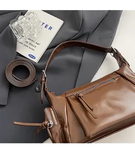 Détail de la bandoulière réglable et du zip argenté sur le sac polochon en cuir marron brillant