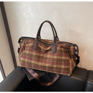 Détail du sac de voyage à carreaux avec poignées en cuir sur un canapé chic