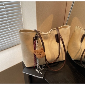 Detail of cream tote bag with brown handles, plush bear charm, and metal zipper closure