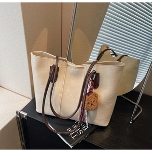 Close-up of beige tote bag with brown straps, gold zipper, and cute bear charm detail