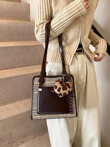 Contrast color brown leather and plaid tote bag with leopard heart charm on models shoulder