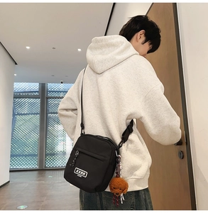 Détail d'un sac bandoulière en nylon noir avec étiquette mode et breloque caniche marron