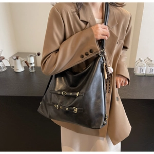 Detail of a large black hobo tote bag featuring decorative straps and a baseball glove charm