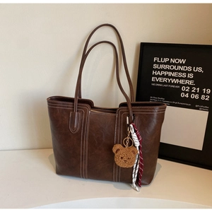 Detail of dark brown tote bag featuring white contrast stitching and plush bear charm