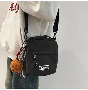 Détail du sac bandoulière en toile noire avec sangle réglable et charm d'ours en peluche