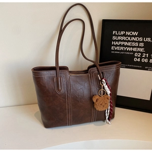 Close-up of a dark brown tote bag with white stitching and a cute bear charm