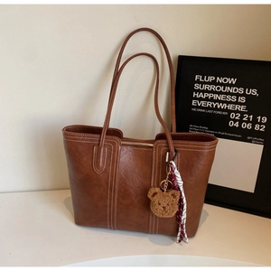 Brown tote bag detail with white contrast stitching and a cute plush bear pendant