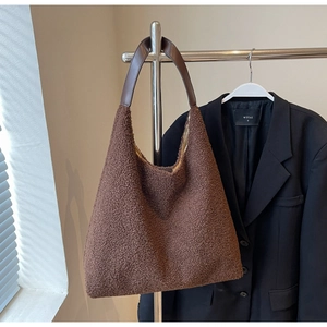 Détail d'un sac cabas en peluche marron avec anse en cuir suspendu sur un cintre