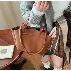 Detail of brown lychee leather tote bag with contrast white stitching and dual handles