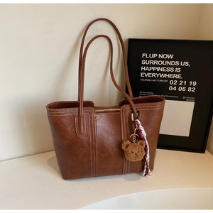 Close-up of brown tote bag with white stitching, teddy bear charm, and silk ribbon