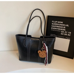 Detail of black faux leather tote bag with white contrast stitching and plush bear charm